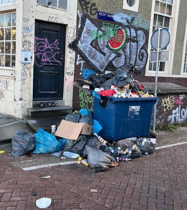 Overflowing waste container surrounded by rubbish bags on a city street