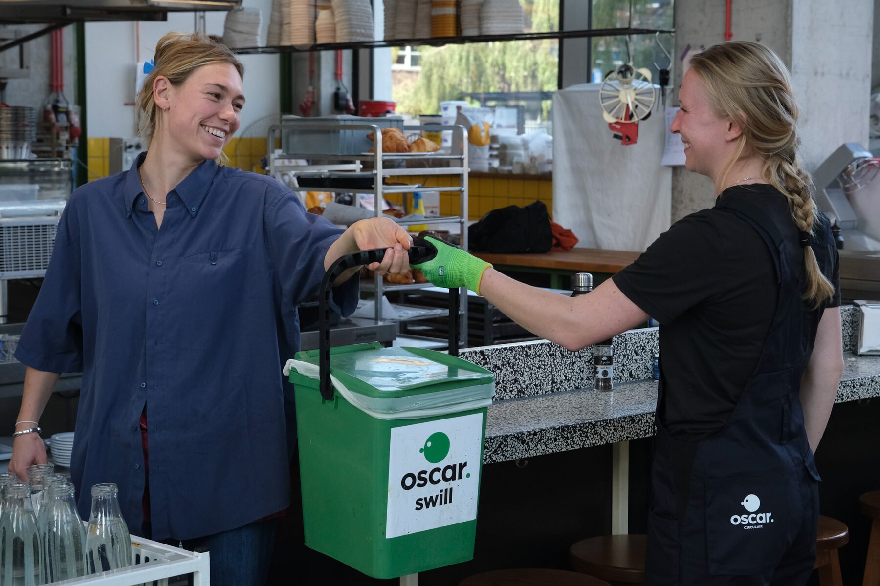 An Oscar Circulair collector handing over a green Oscar swill bin to a hospitality worker